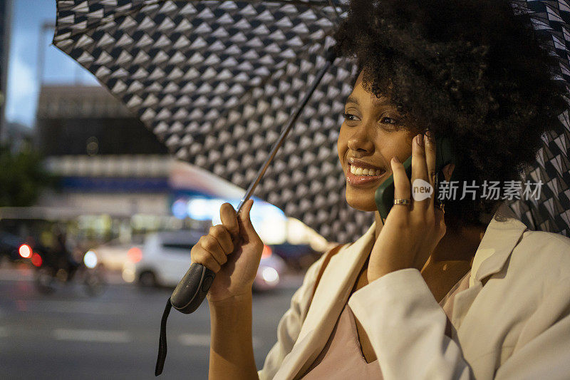 在圣保罗大道(Avenida Paulista)，一名女子打着雨伞用智能手机聊天，São Paulo，巴西。